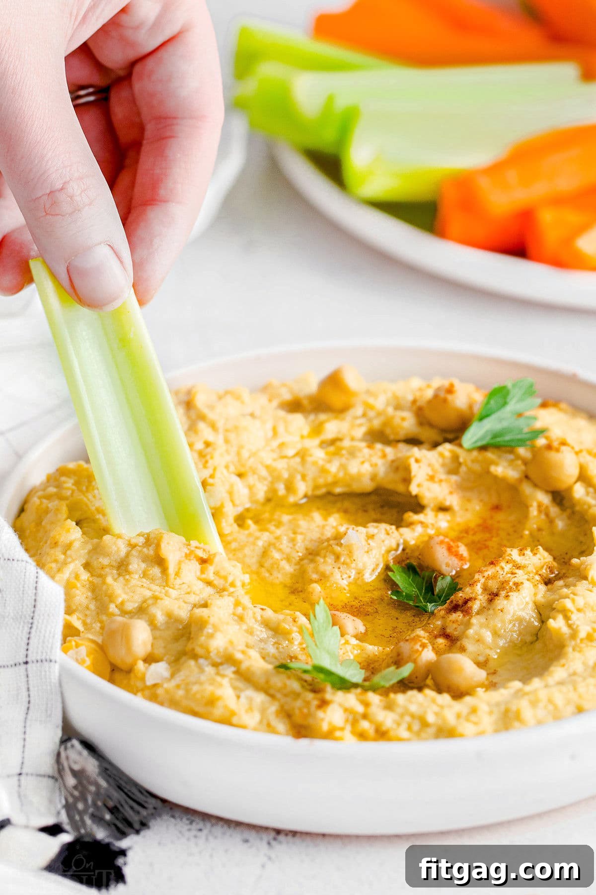 A crisp celery stick being dipped into a bowl of creamy homemade hummus, showcasing its perfect texture and inviting appeal.