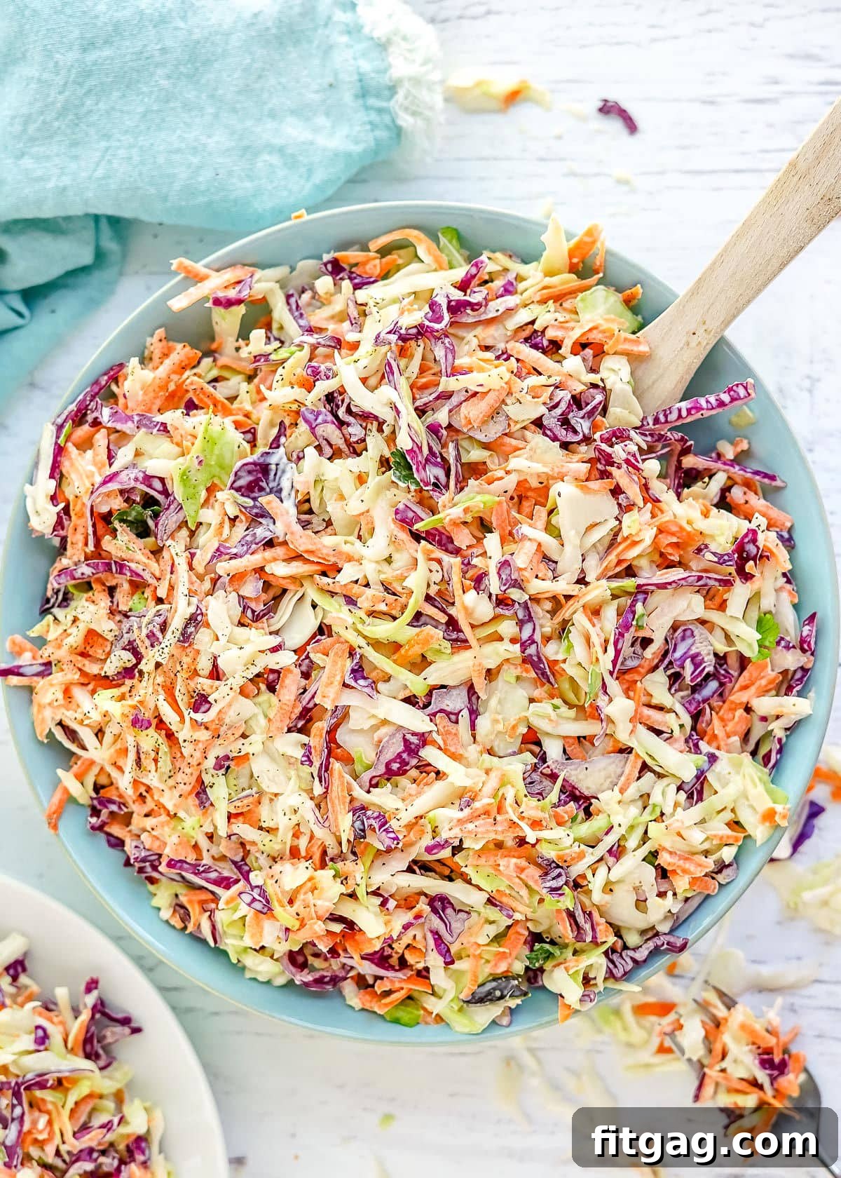 Vibrant coleslaw prepared in a light blue bowl with a wooden spoon, showcasing its fresh ingredients and creamy texture.