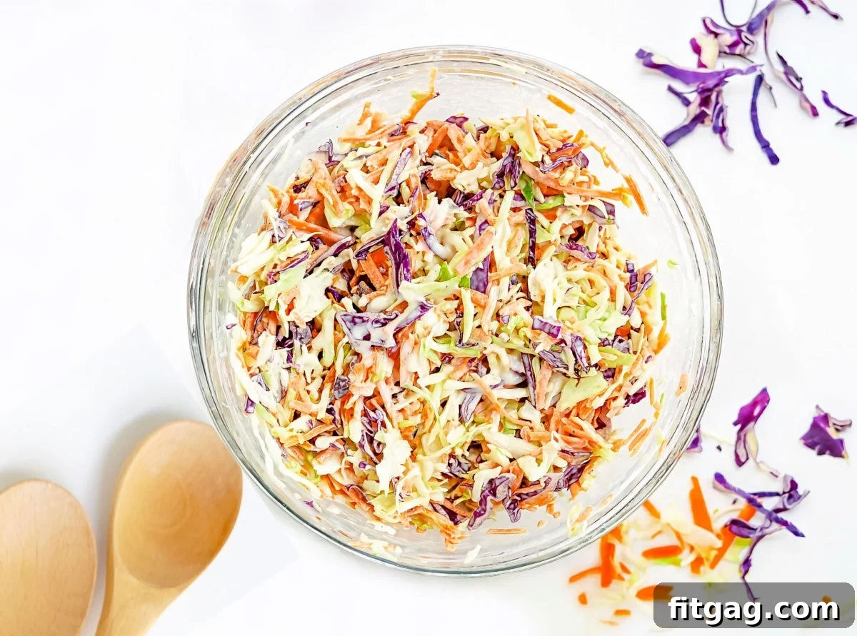 Creamy coleslaw recipe tossed together in a clear glass mixing bowl, highlighting its perfect consistency.