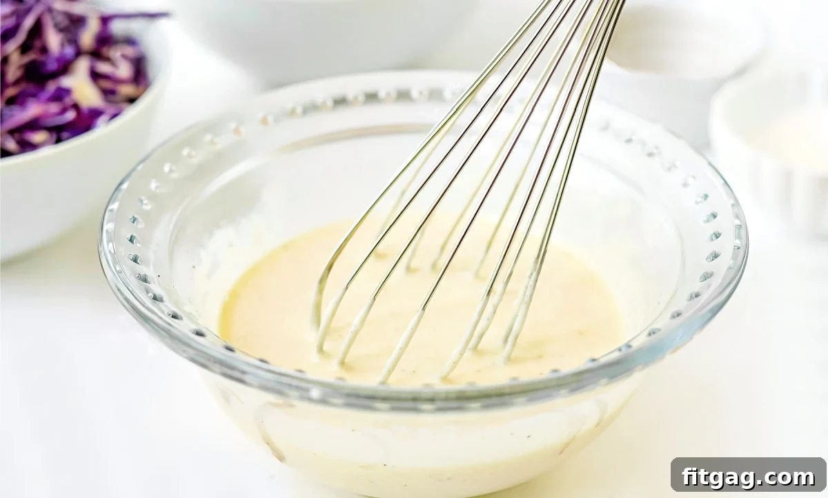 Coleslaw dressing prepared in a glass bowl with a whisk, ready to be combined with the vegetables.