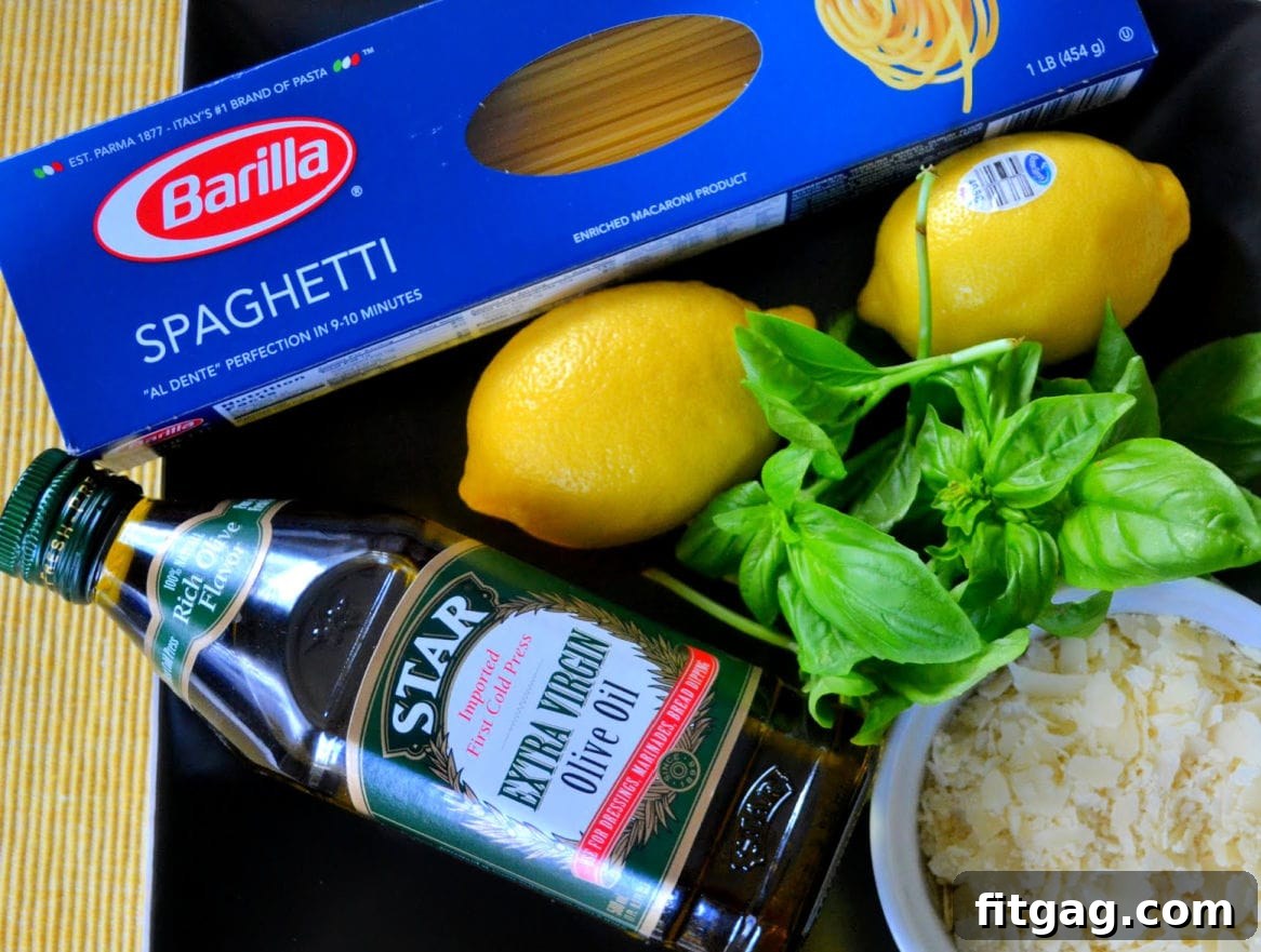 A flat lay image displaying all the fresh ingredients for Lemon Spaghetti, including spaghetti noodles, lemons, a bottle of olive oil, a block of Parmigiano-Reggiano cheese, basil, salt, and pepper.