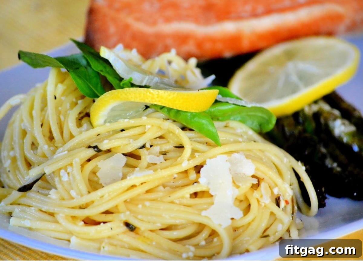 A gourmet plate of Lemon Spaghetti served with asparagus and salmon, elegantly garnished with a lemon wedge, fresh basil, and grated Parmesan cheese.