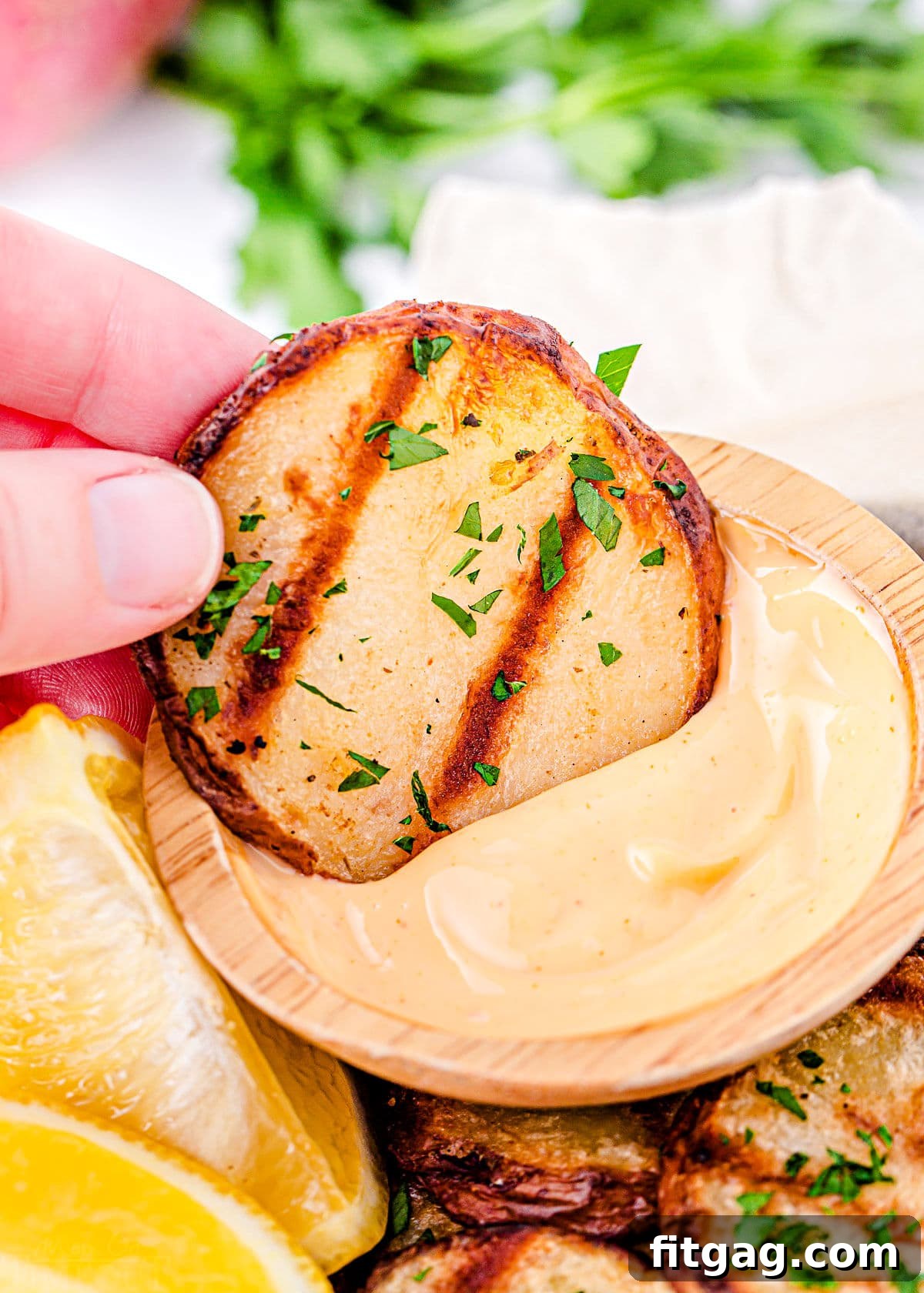 Smoky Garlic Herb Potatoes 3 A perfectly grilled potato slice being dipped into a creamy, spicy mayo sauce, highlighting its golden brown char marks.
