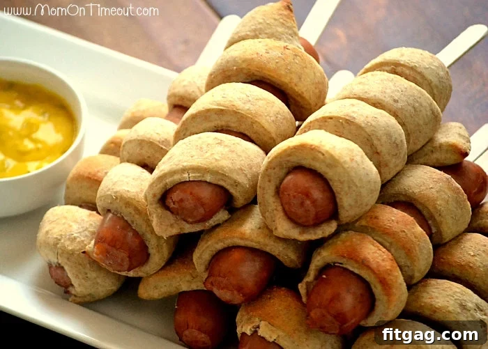 A plate of freshly baked Spiral-Wrapped Sausages on a Stick with a side of dipping sauce, highlighting the finished appetizer.