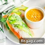 Spring rolls on a white plate with a small bowl of peanut sauce to dip in on the side.