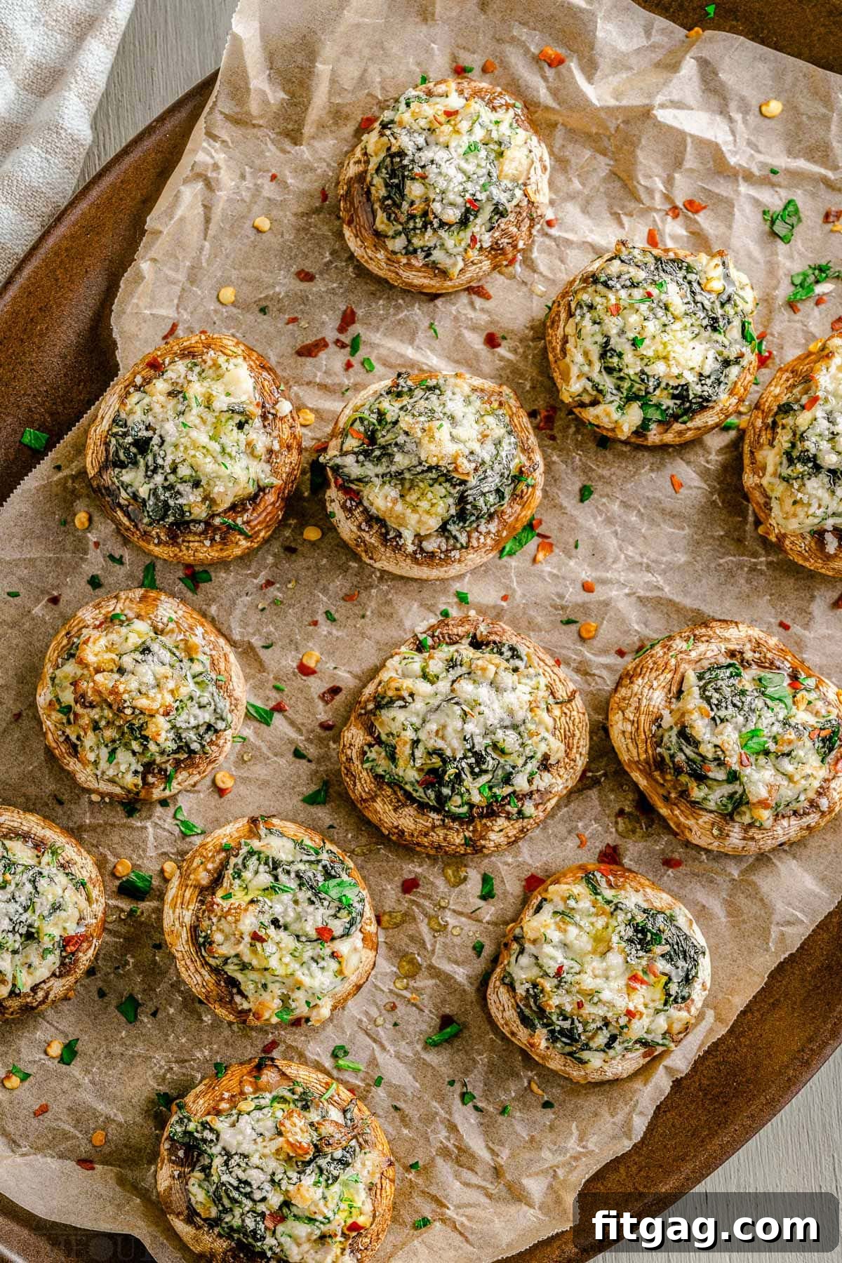 Irresistible Stuffed Mushrooms 3 A baking tray filled with golden brown stuffed mushrooms, garnished with fresh parsley and resting on crumpled brown parchment paper.