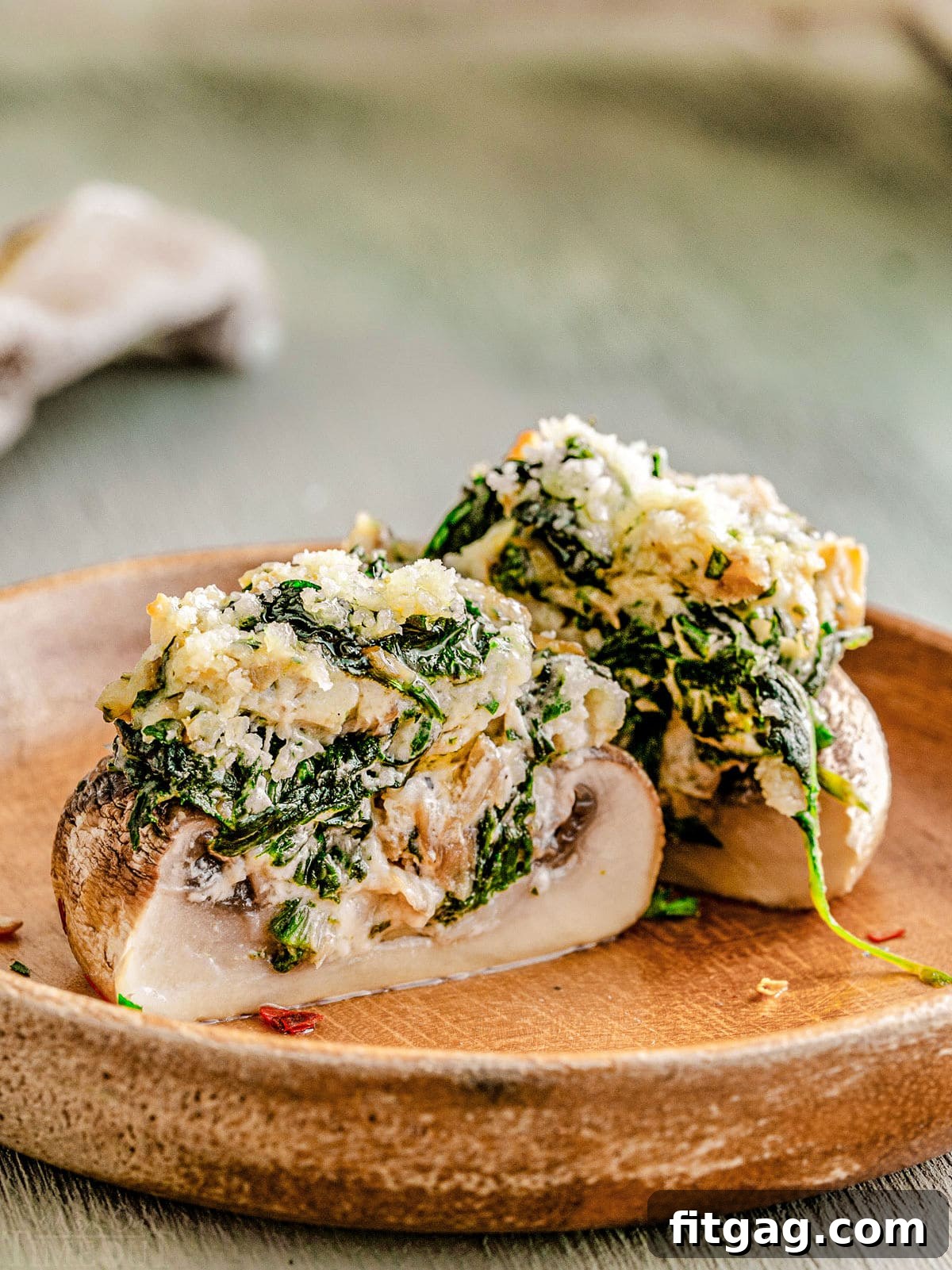 Irresistible Stuffed Mushrooms 6 A perfectly halved stuffed mushroom on a brown plate, showcasing its creamy spinach and cheese filling.