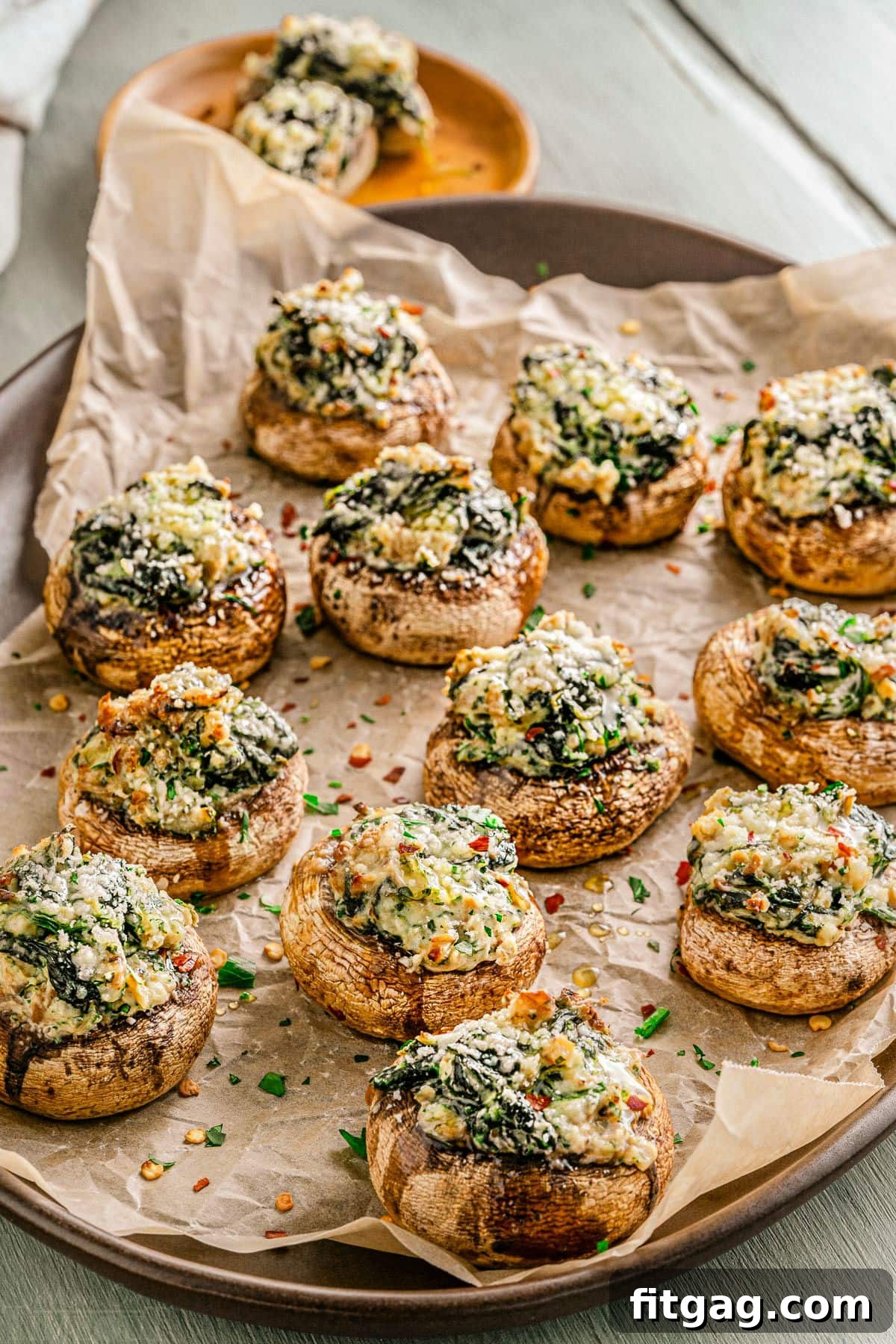 Irresistible Stuffed Mushrooms 7 A baking tray filled with golden brown stuffed mushrooms, garnished with fresh parsley and resting on crumpled brown parchment paper.