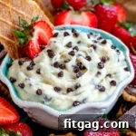 cannoli dip with chocolate chips sprinkled on top in a small white bowl with blue interior surrounded by cookies and strawberries ready to be enjoyed.