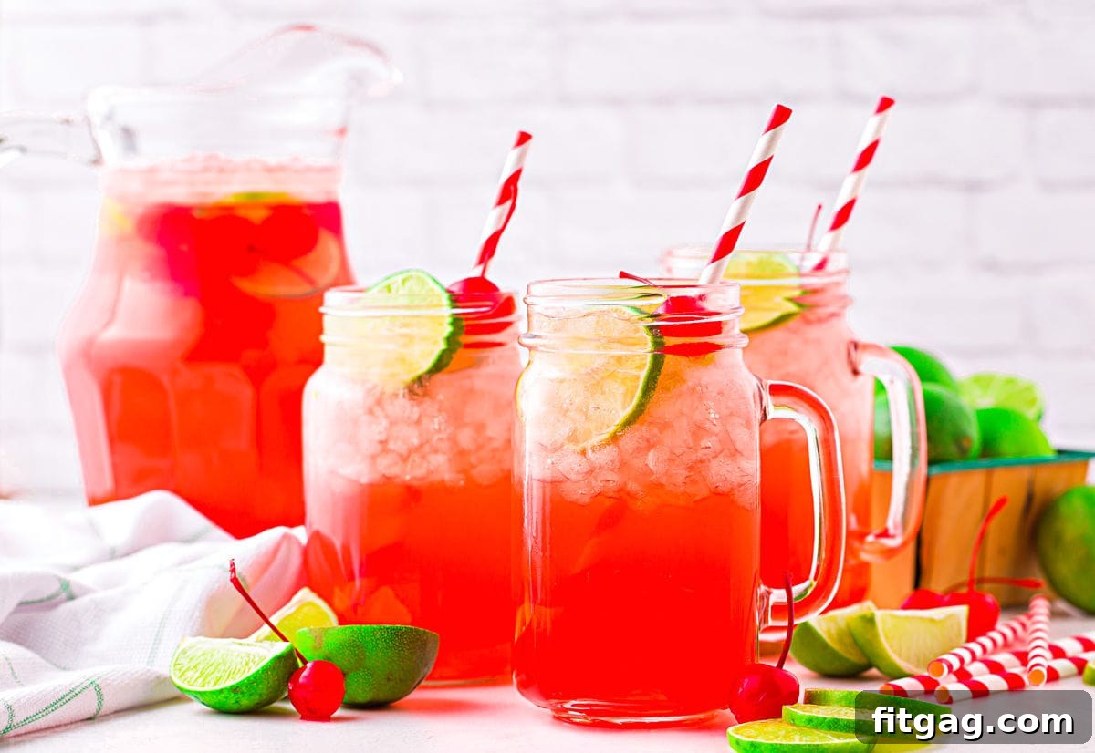 An inviting arrangement of three mason jars and a tall glass pitcher, all generously filled with sparkling cherry limeade. Each serving is elegantly garnished with fresh lime slices and bright red maraschino cherries, creating a festive and colorful display.