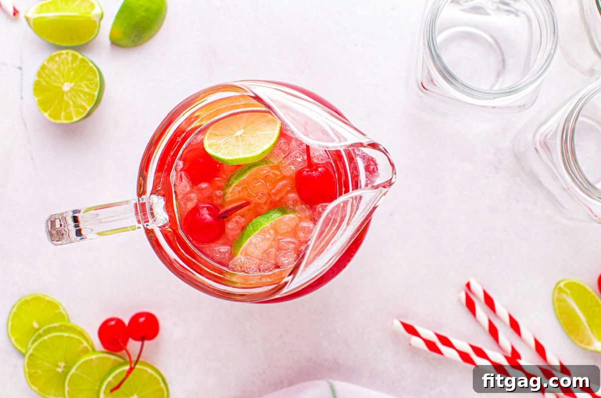A high-angle, top-down perspective captures various ingredients being meticulously added into a large glass pitcher. This image visually illustrates the initial, crucial steps of the cherry limeade preparation process, highlighting the fresh components.