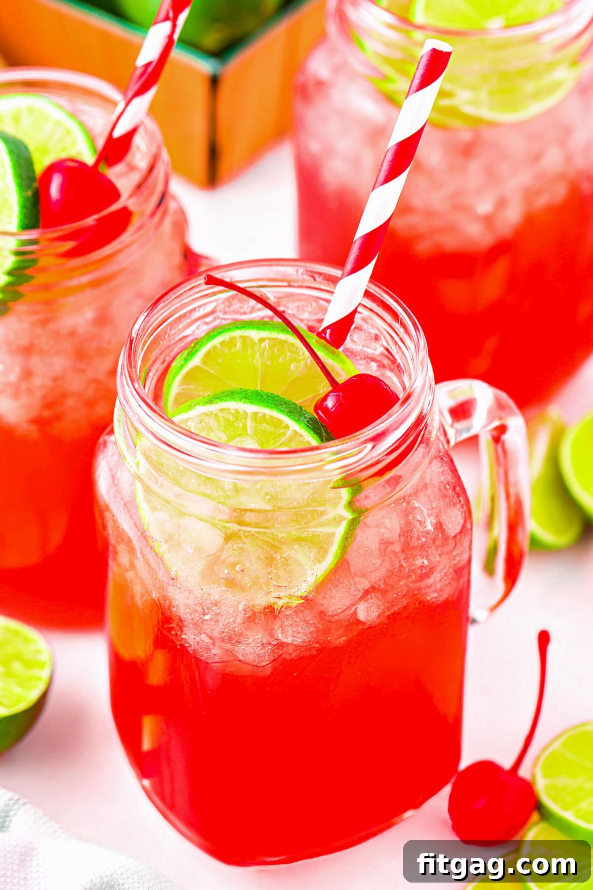 A close-up view of a perfectly prepared copycat Sonic cherry limeade, served elegantly in individual mason jar glasses. Each glass is meticulously garnished with fresh lime slices and a bright maraschino cherry, inviting immediate enjoyment and a refreshing sip.