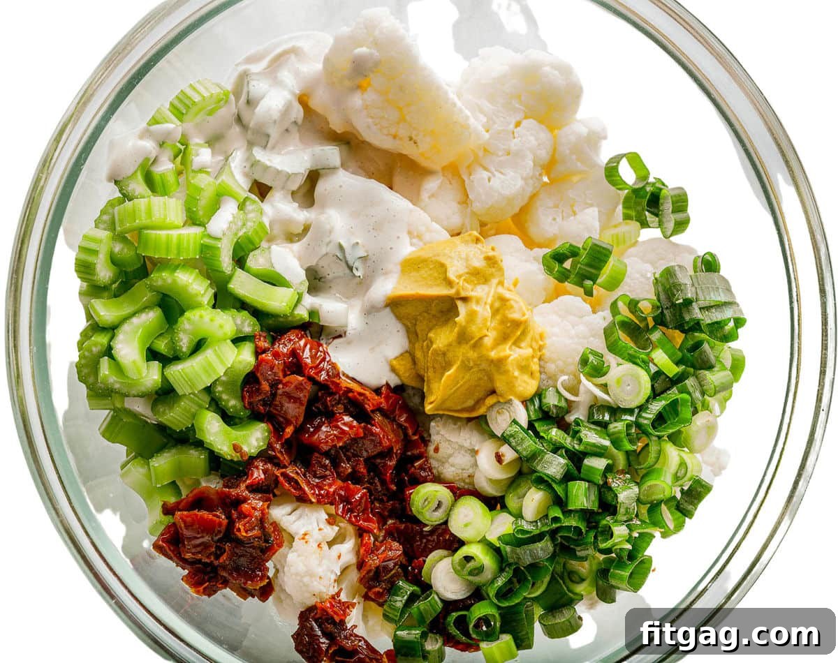 All salad ingredients in a large glass bowl, ready to be gently mixed together to create the cauliflower salad.
