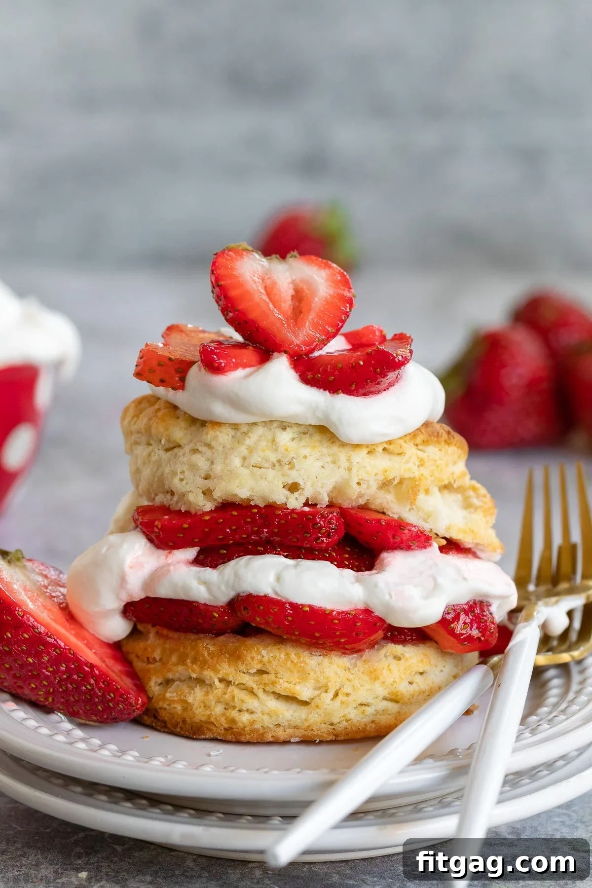 Homemade strawberry shortcake featuring layers of split biscuit, macerated strawberries, and freshly whipped cream, presented on a white plate.