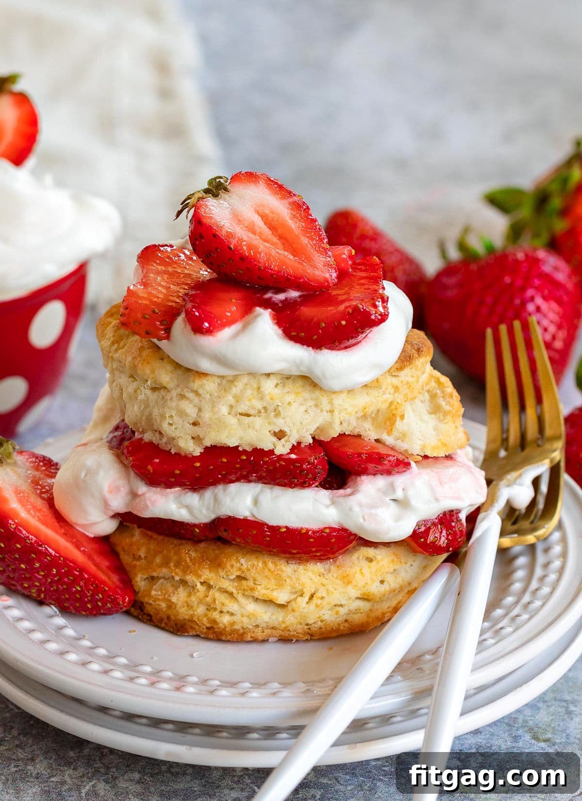 A beautifully assembled strawberry shortcake on a white plate, showcasing distinct layers of macerated strawberries and freshly whipped cream, with two forks poised at the side.