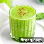 simple green smoothie recipe in glass sitting on small white plate in front of blender.