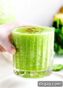 The Perfect Green Smoothie 10 hand holding green smoothie in ridged glass with greens in the background.