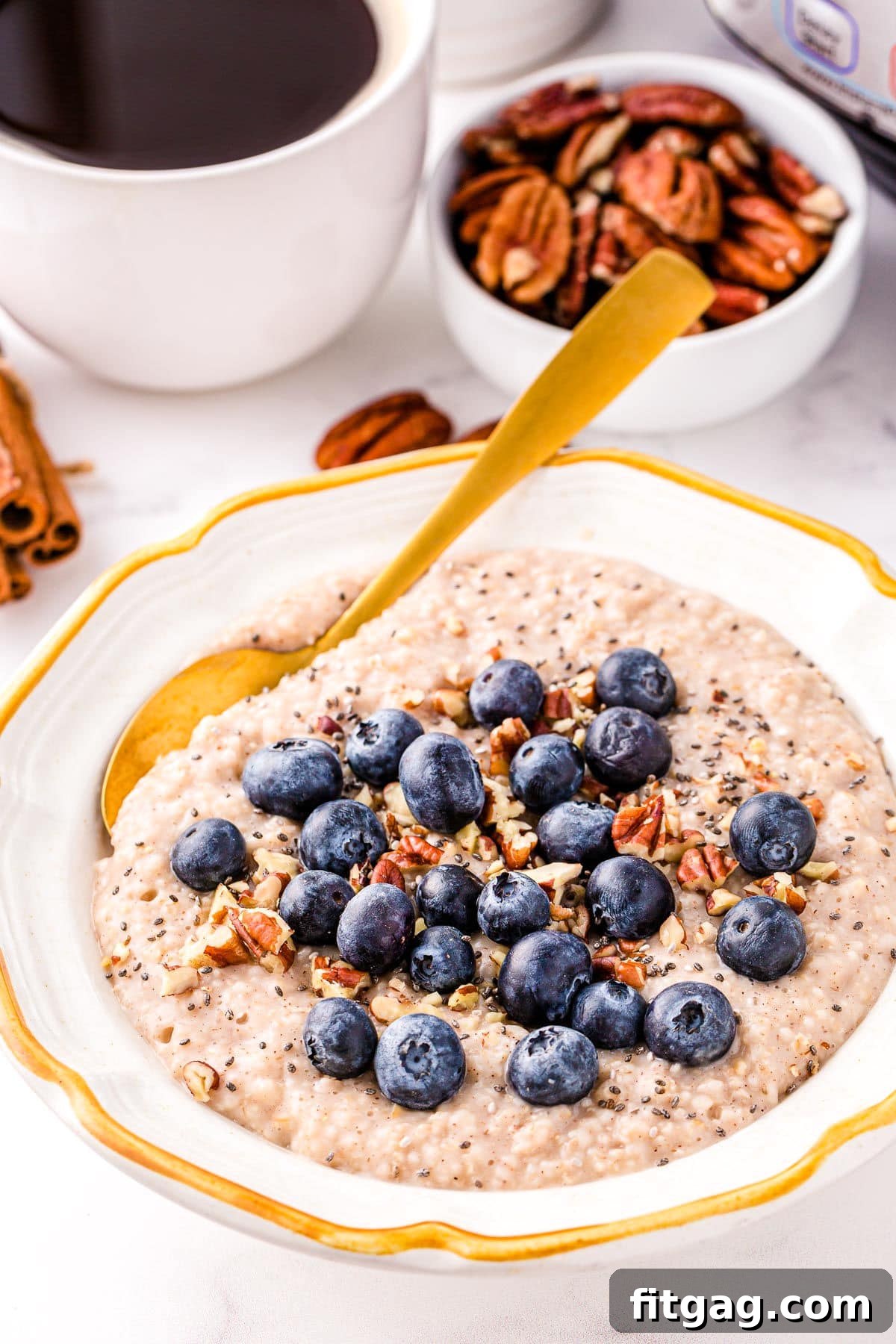 Foolproof Instant Pot Steel Cut Oats 3 instant pot oats in white bowl with gold rim topped with blueberries and ground cinnamon. cup of coffee and small bowl of pecans in background.
