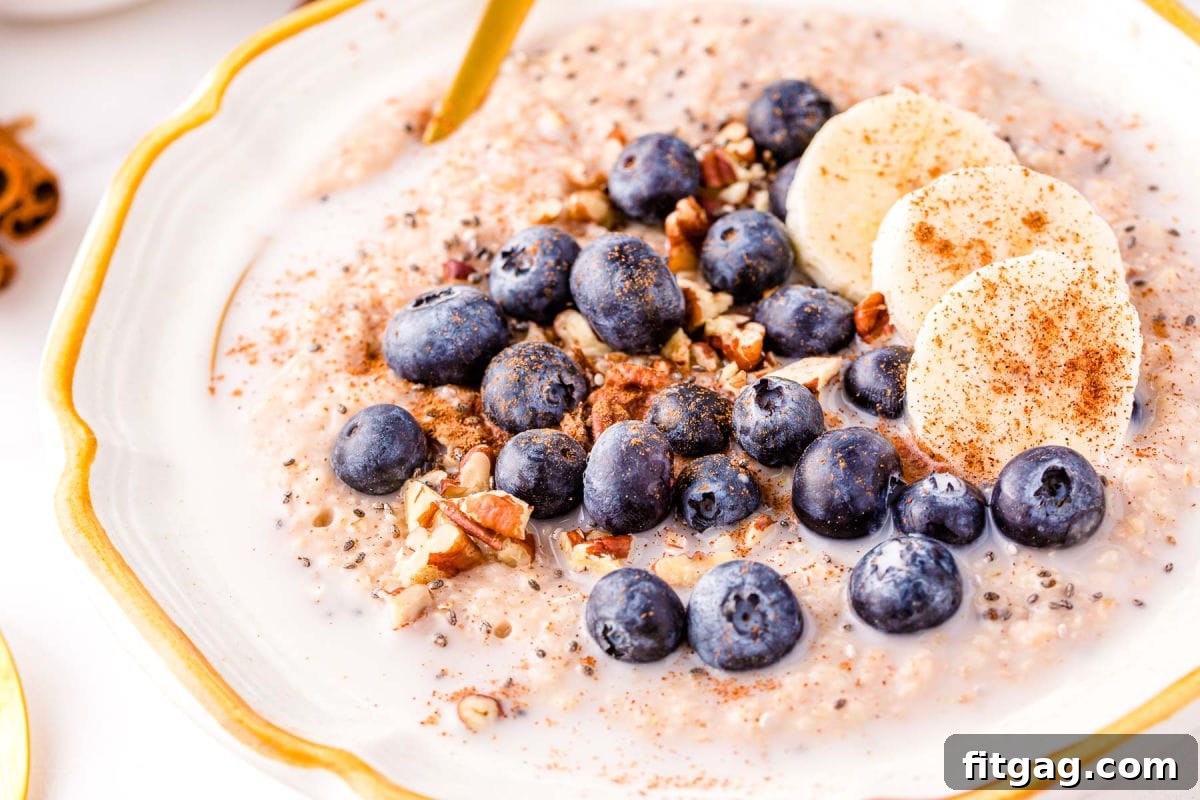 Creamy Instant Pot Steel Cut Oats 4 steel cut oatmeal topped with blueberries, pecans and cinnamon in a white bowl with a gold spoon.