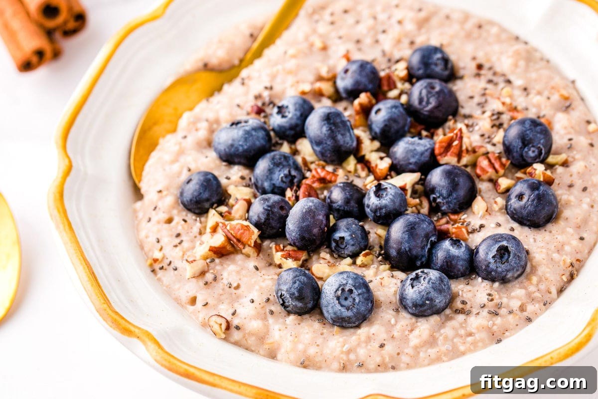 Foolproof Instant Pot Steel Cut Oats 7 steel cut oatmeal topped with blueberries, pecans and cinnamon in a white bowl with a gold spoon.