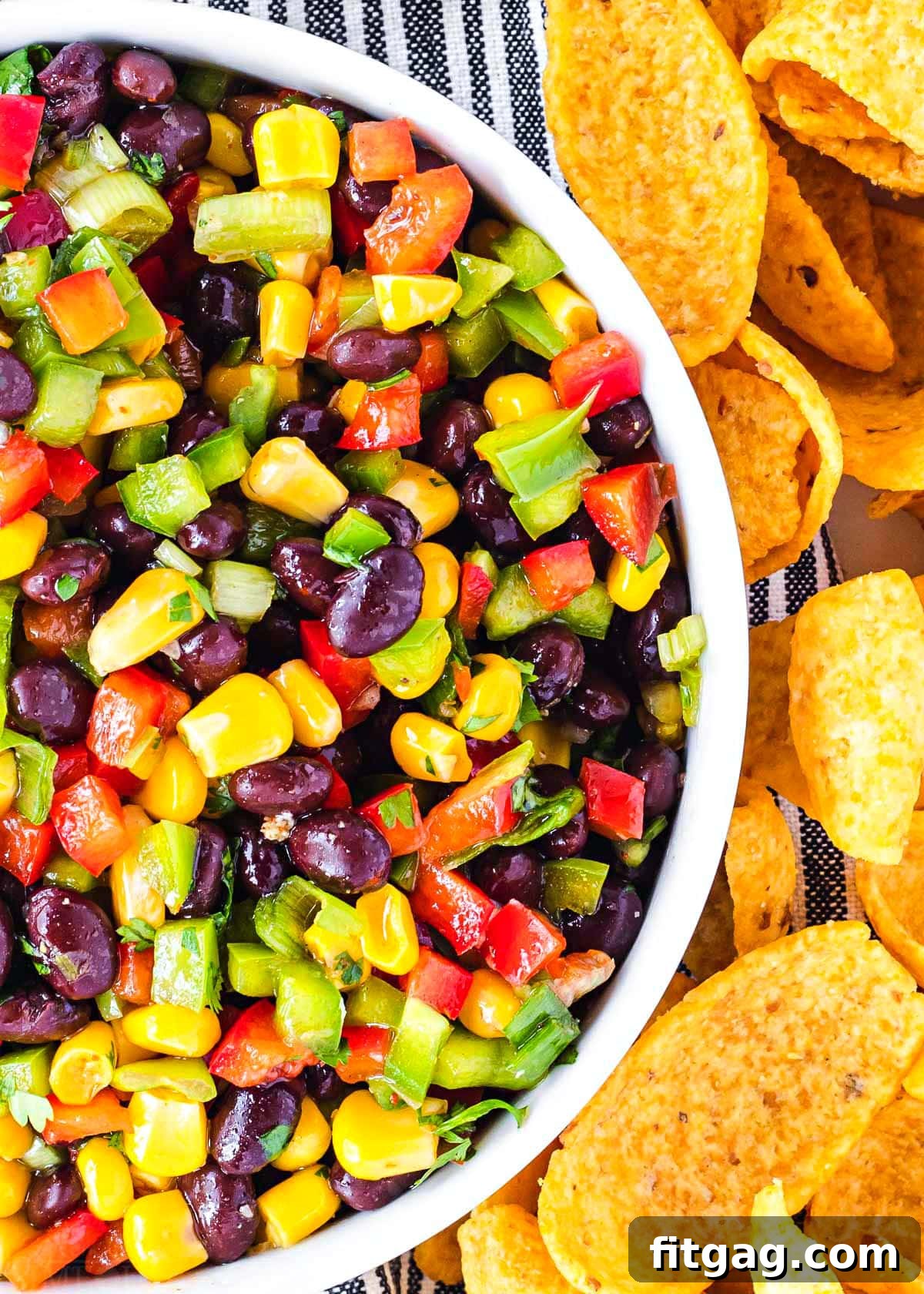 Close-up view of vibrant black bean and corn salsa in a white bowl, surrounded by corn chips.