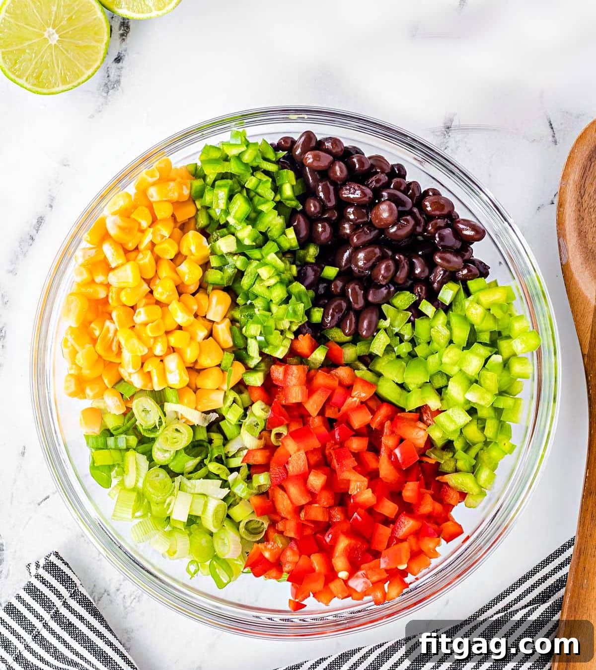 Prepped black bean and corn salsa ingredients in a clear glass bowl, ready for mixing.