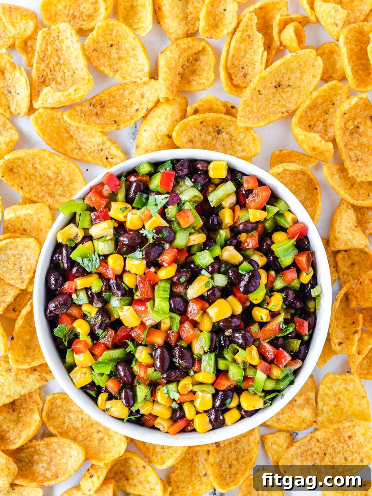 Black bean corn salsa in a small white serving bowl, surrounded by large corn chips, ready to be enjoyed.