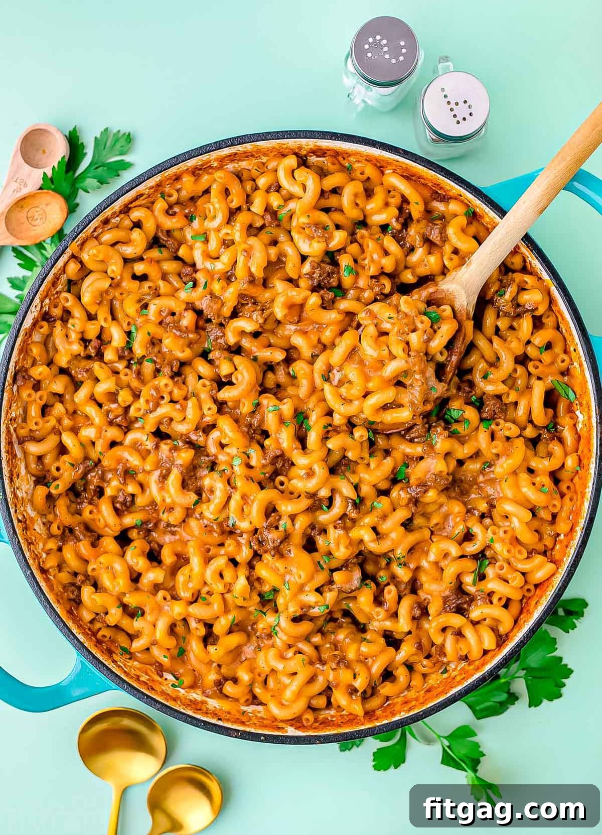 skillet of homemade hamburger helper garnished with chopped fresh parsley. background is light aqua colored.