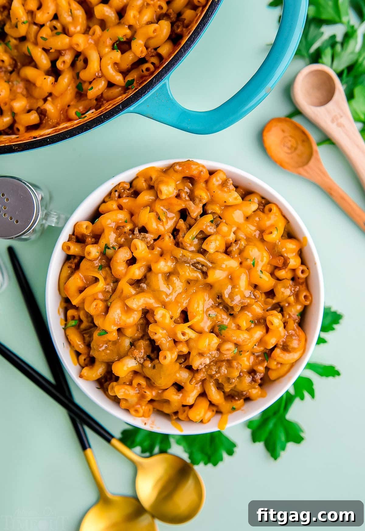 top down look at bowl of hamburger helper sitting next to skillet with the rest of it. light green background. 