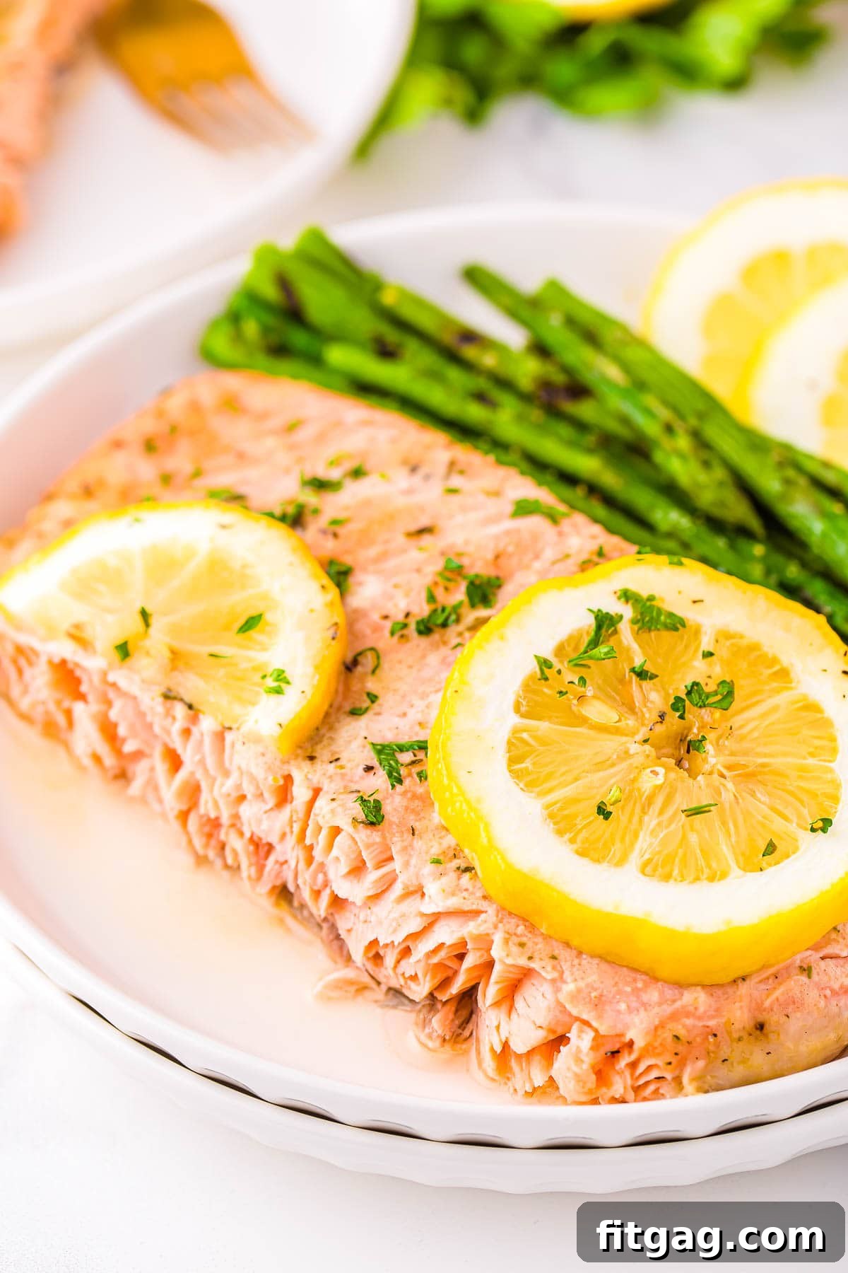 A perfectly cooked piece of baked salmon, served on a white plate with tender asparagus and fresh lemon slices.