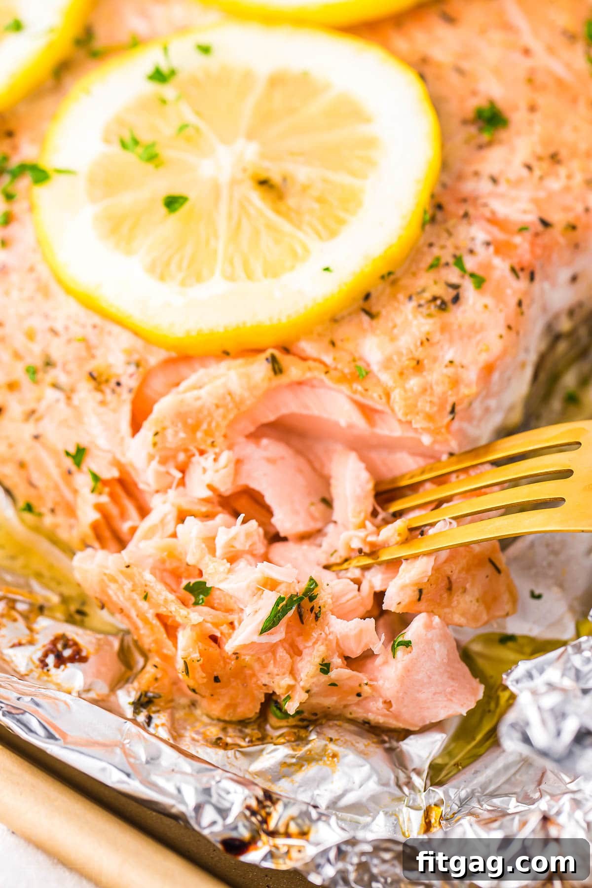 A golden fork gently flaking a tender, perfectly cooked salmon fillet, topped with a vibrant lemon slice.