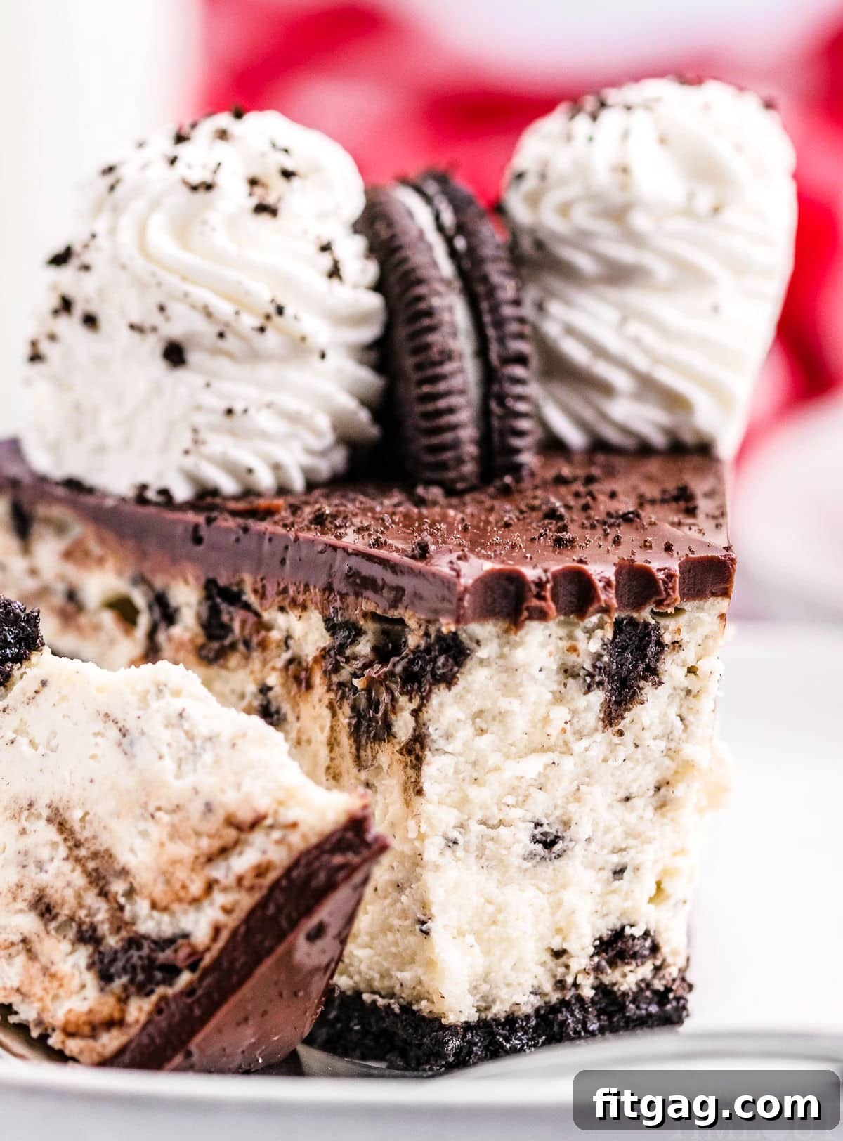 Ultimate Oreo Cheesecake 2 A close-up view of a slice of rich, creamy Oreo cheesecake, showing the distinct layers of Oreo crust, cheesecake filling with cookie pieces, and a glossy chocolate ganache topping. A bite has been taken from the slice, revealing its luscious texture.