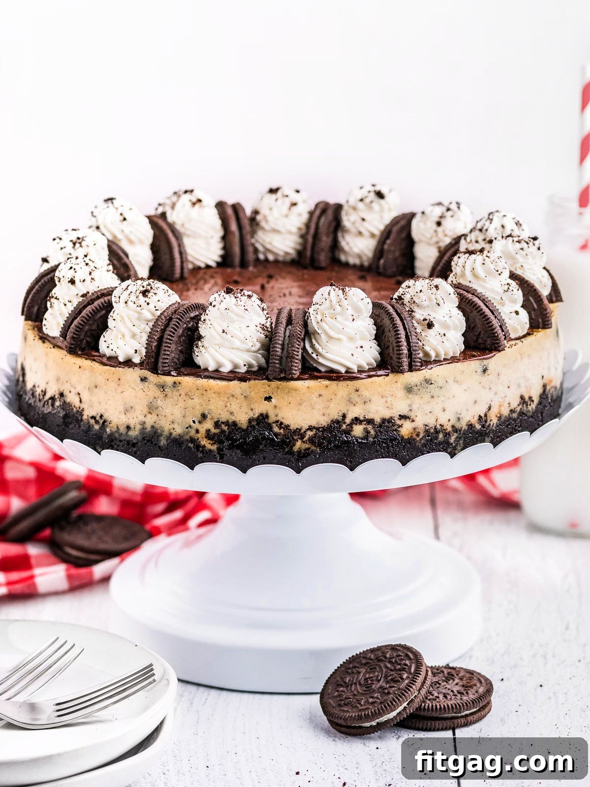 Ultimate Oreo Cheesecake 4 A stunning whole Oreo cheesecake, lavishly topped with swirls of whipped cream and perfectly placed Oreo cookies, displayed on an elegant white metal cake stand, ready to be served and admired.