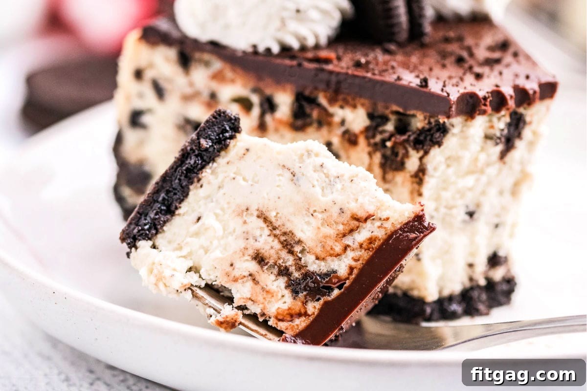 Ultimate Oreo Cheesecake 8 A delectable bite of Oreo cheesecake is positioned beside a full slice on a pristine white plate, showcasing the dessert's appealing texture and inviting presentation.