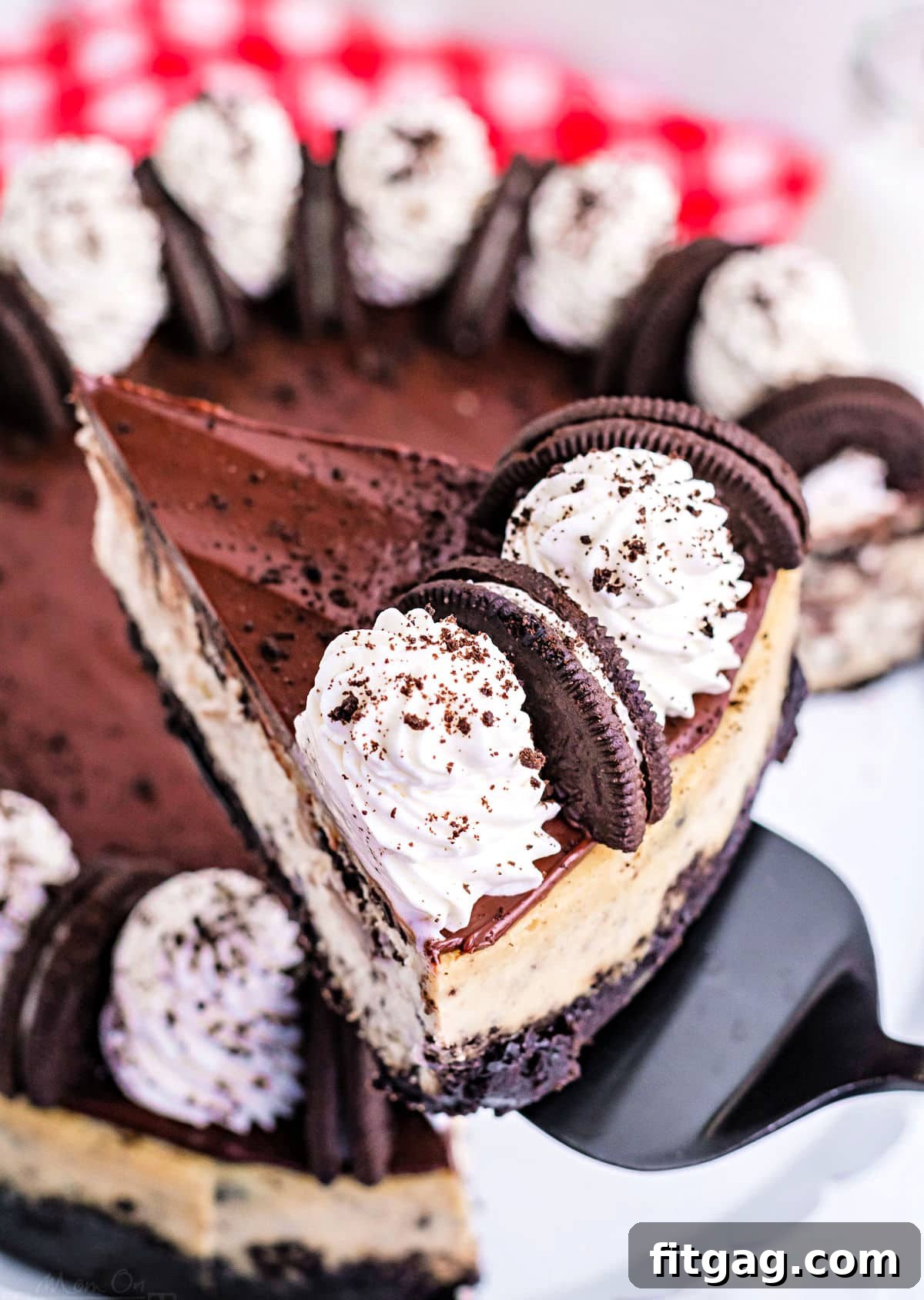 Ultimate Oreo Cheesecake 9 A hand elegantly holds a pristine slice of Oreo cheesecake, lifted above the remaining cheesecake on a serving plate, highlighting its rich layers and tempting texture before it's enjoyed.