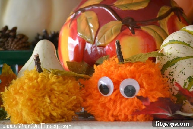 A close-up of a finished pom pom pumpkin with googly eyes and a green leaf, showcasing a cute and simple Halloween decoration.