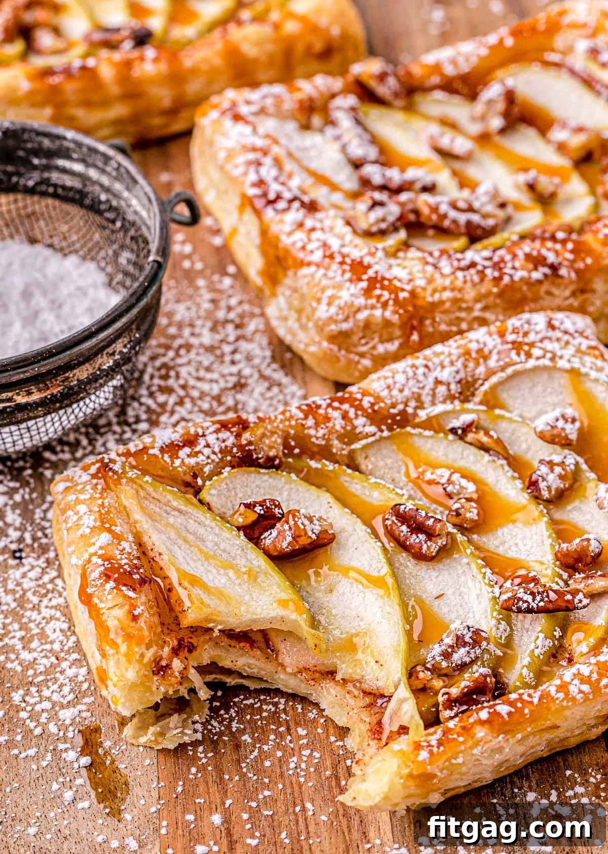 Effortless Caramel Apple Tart 2 apple tart drizzled with caramel sauce and dusted with powdered sugar on a wood cutting board.