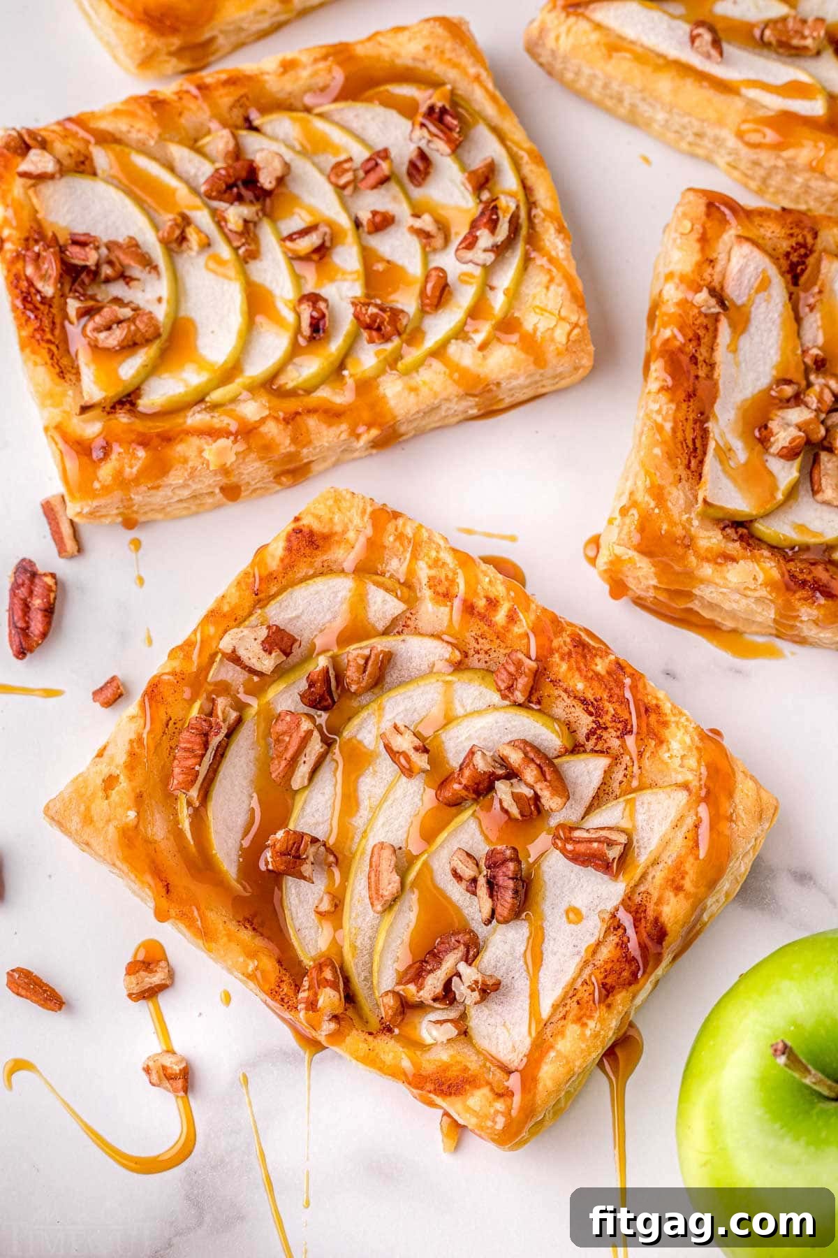 Effortless Caramel Apple Tart 3 puff pastry apple tart recipe sitting on marble surface with drizzle of caramel sauce.