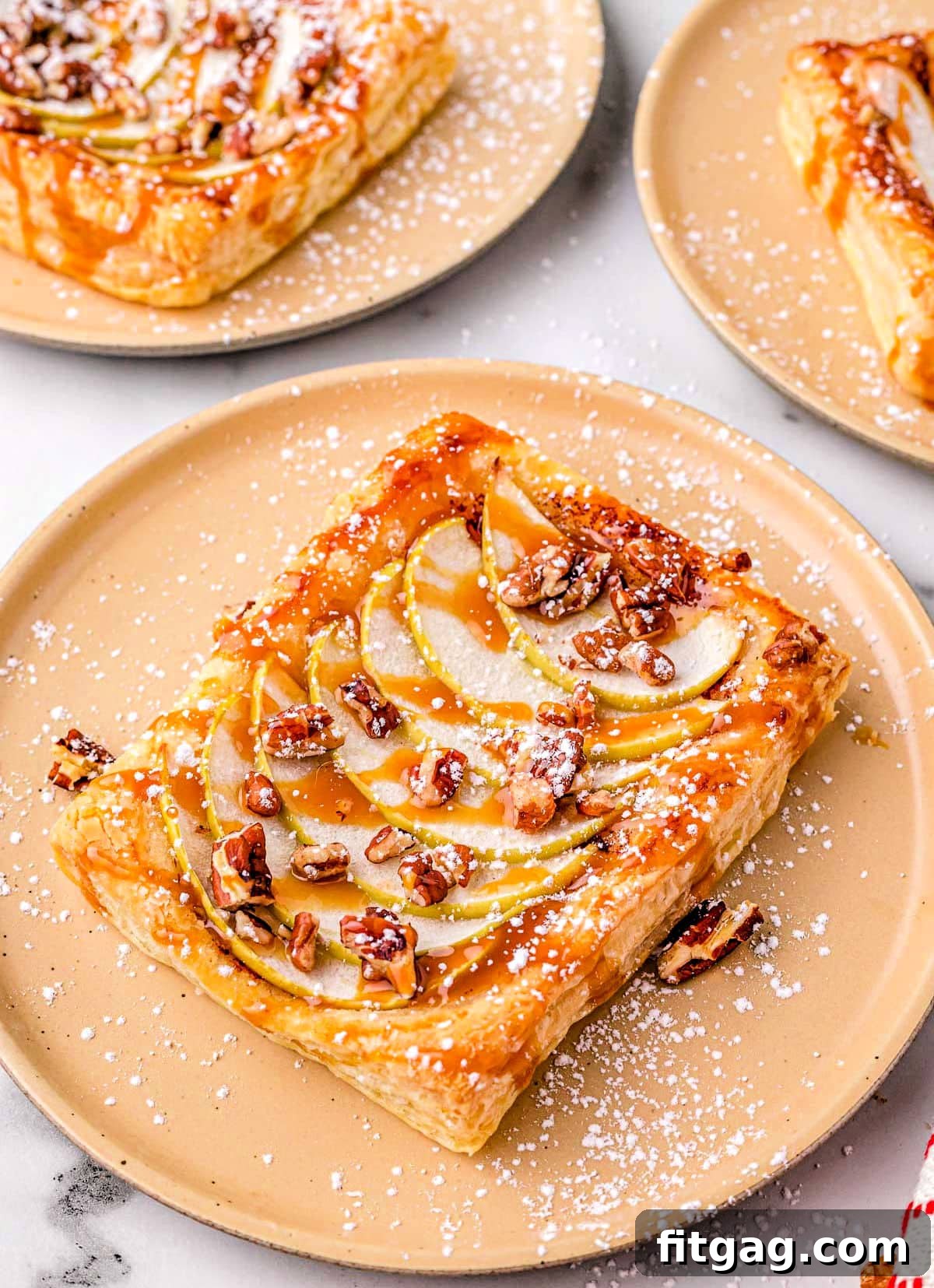 Effortless Caramel Apple Tart 4 single apple tart on light orange plate with two more apple tarts in the background.