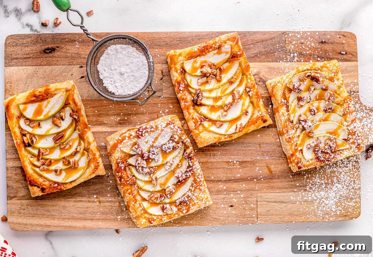 Effortless Caramel Apple Tart 7 four apple tarts sitting on large wood cutting board drizzled with caramel and sprinkled with powdered sugar.