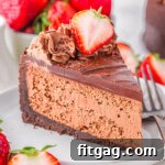 Slice of decadent chocolate cheesecake with an oreo crust and rich chocolate ganache on white round plate. Topped with chocolate shavings and fresh strawberries.
