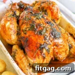 roasted chicken with golden skin and herbs cooked on top sitting in white roasting dish.