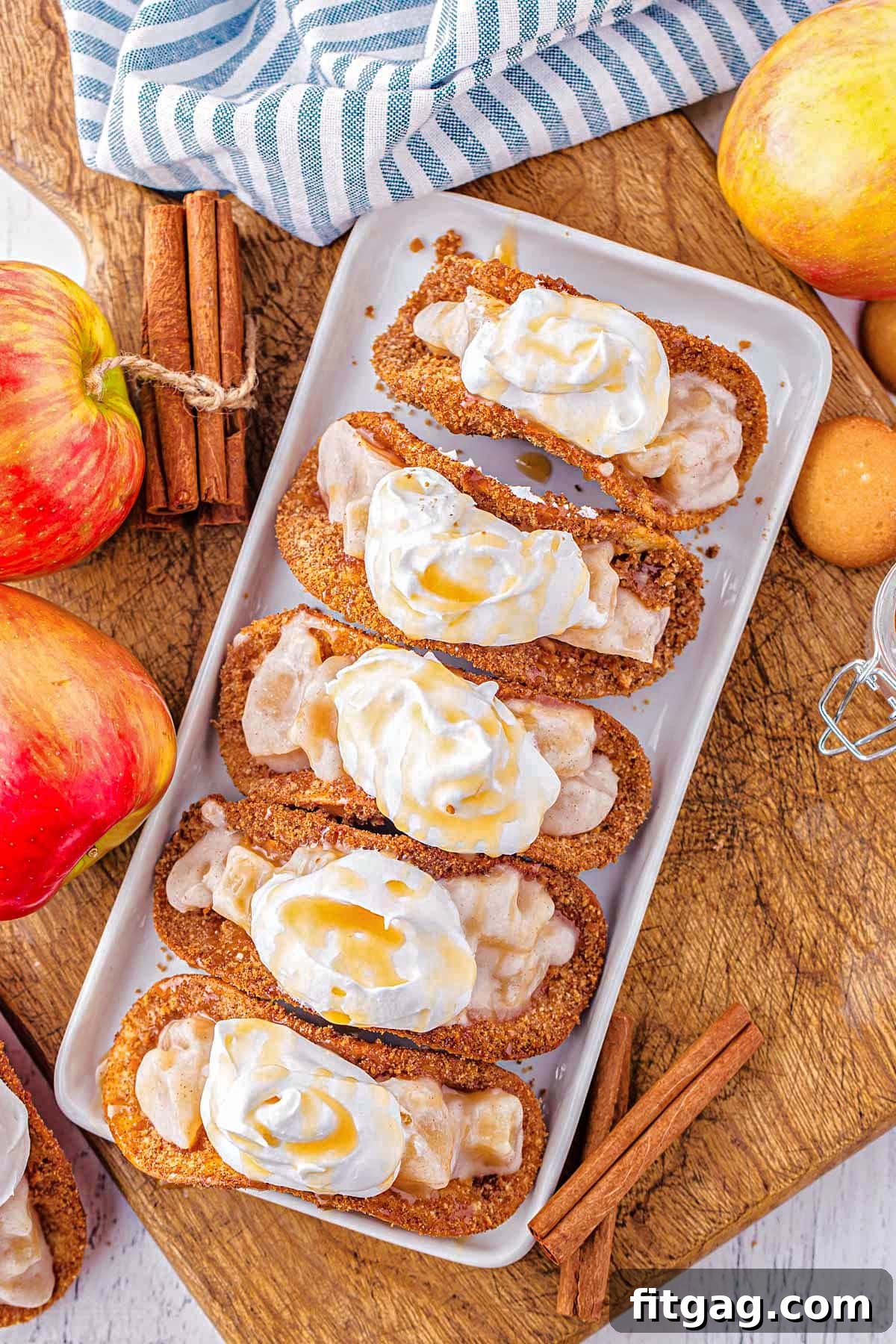 top down view of dessert tacos filled with apple pie filling and topped with whipped cream and caramel all lined up on a white tray ready to serve.