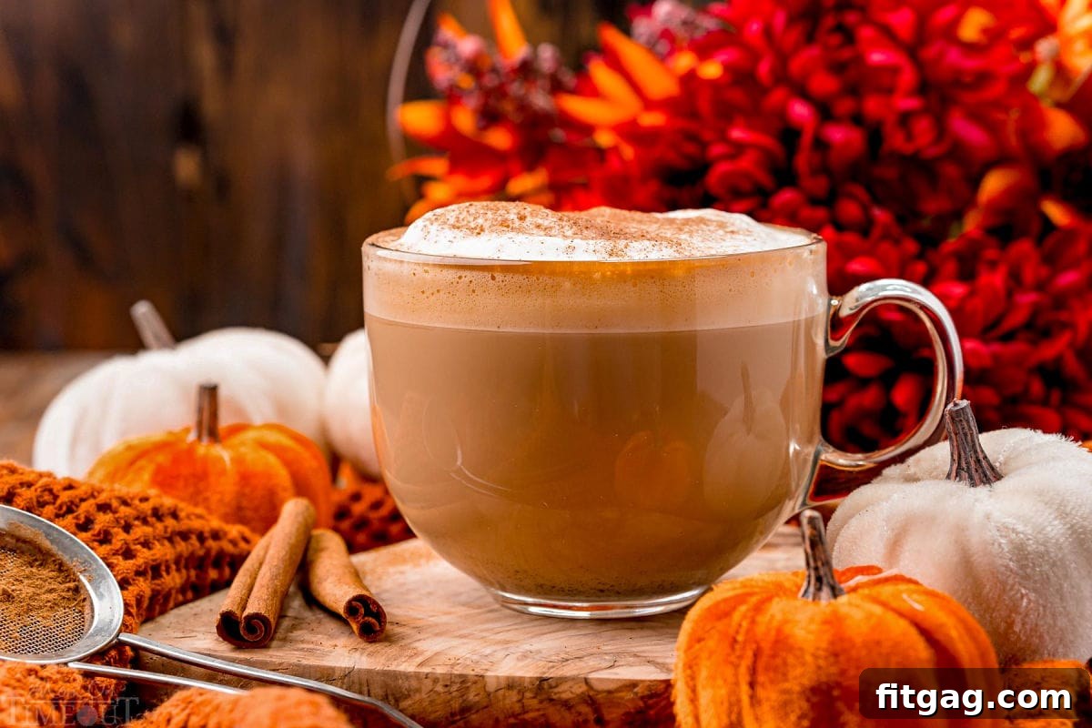 front view of a pumpkin spice latte ready to be enjoyed garnished with pumpkin pie spice and sitting in front of fall colored flowers on a wood board.