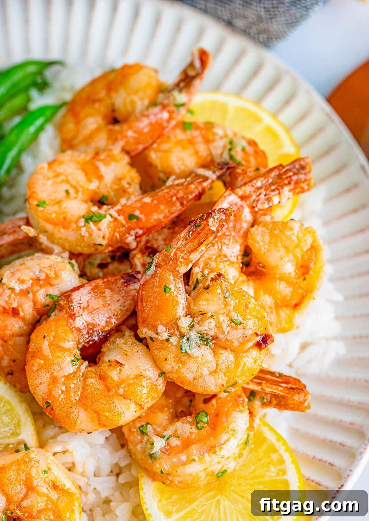 Effortless Air Fryer Shrimp 3 Close-up, top-down view of perfectly cooked air fryer shrimp on a white plate, garnished with lemon wedges and a generous drizzle of savory garlic butter sauce.