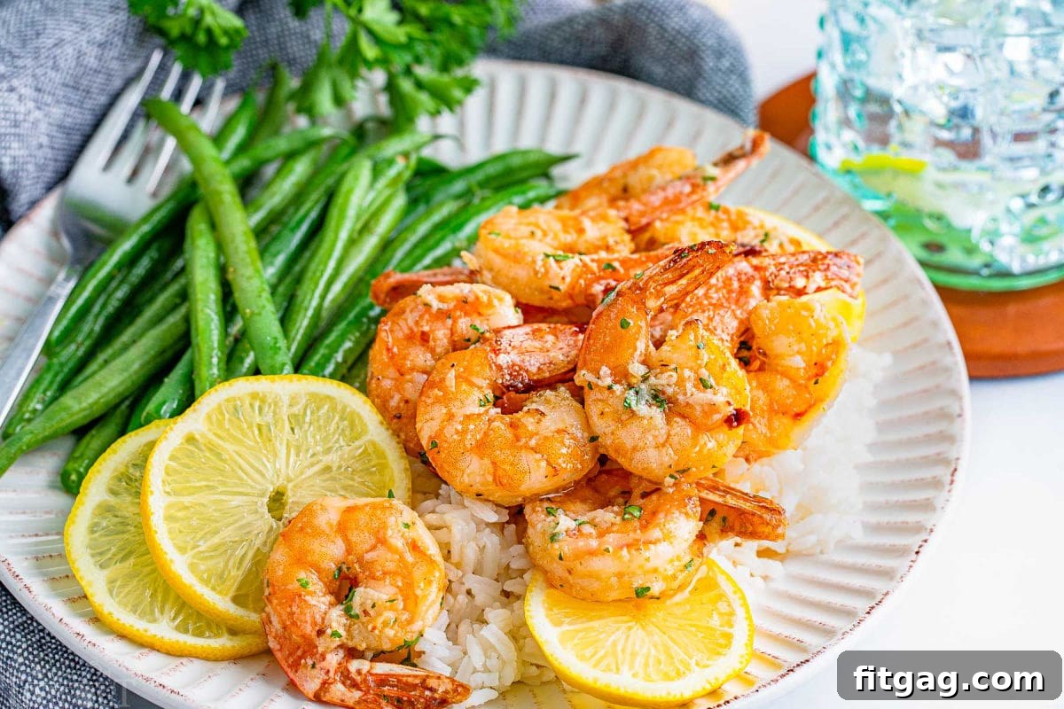 Effortless Air Fryer Shrimp 4 Beautifully arranged air fryer shrimp with garlic herb butter sauce on a scalloped white plate, served with green beans and fresh lemon wedges.