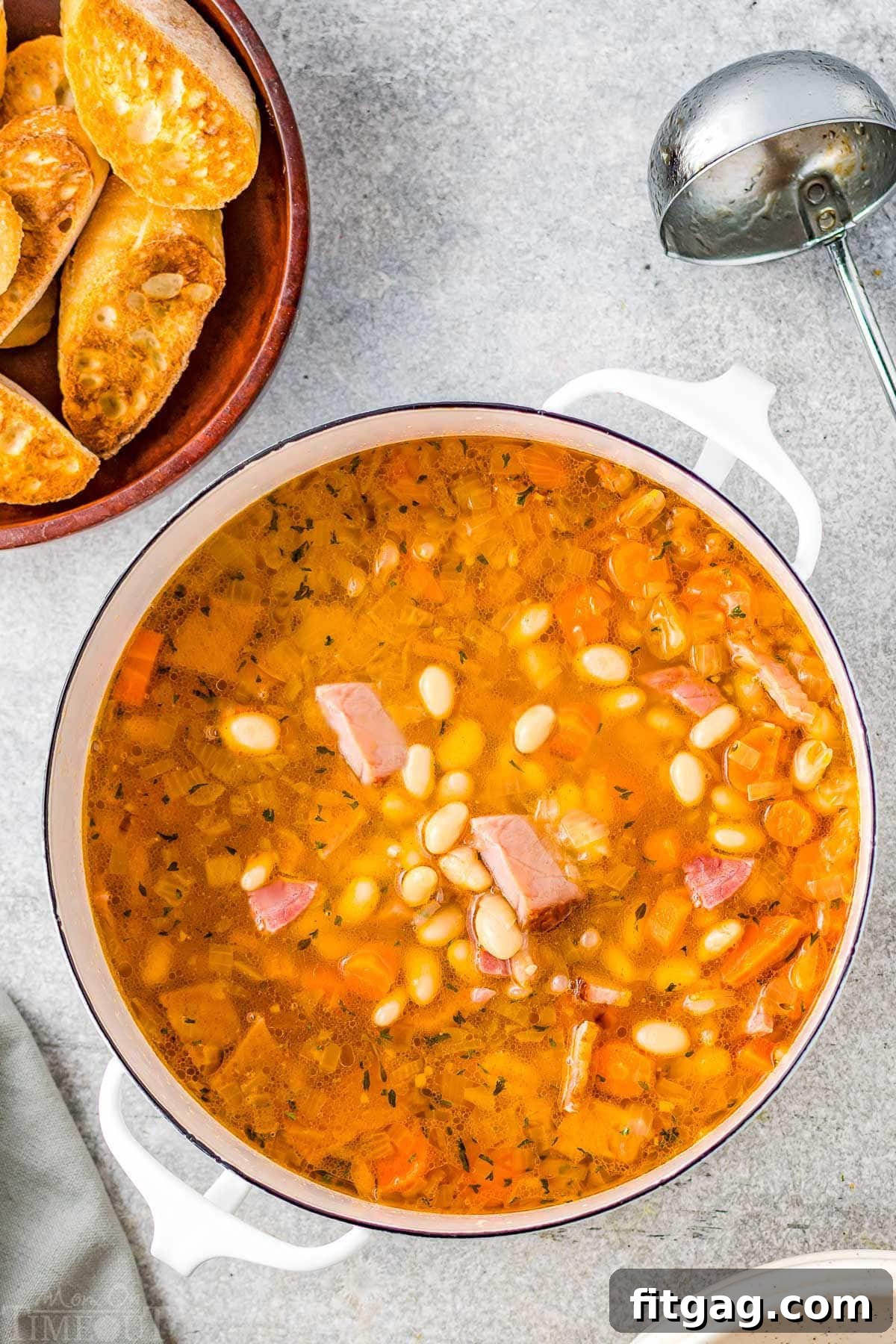 pot full of ham and bean soup with crusty bread in upper left corner on plate.