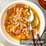 bowl of ham and bean soup with two spoons with wood handles next to pot of soup.