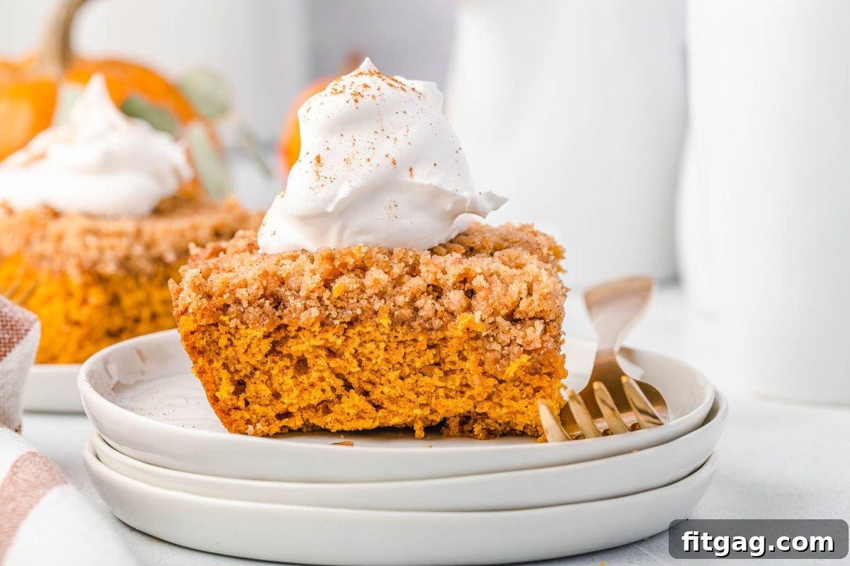 A close-up shot of a magnificent Pumpkin Coffee Cake, generously adorned with a swirl of whipped cream and a delicate dusting of pumpkin pie spice, resting on three elegantly stacked white plates, ready to be enjoyed.