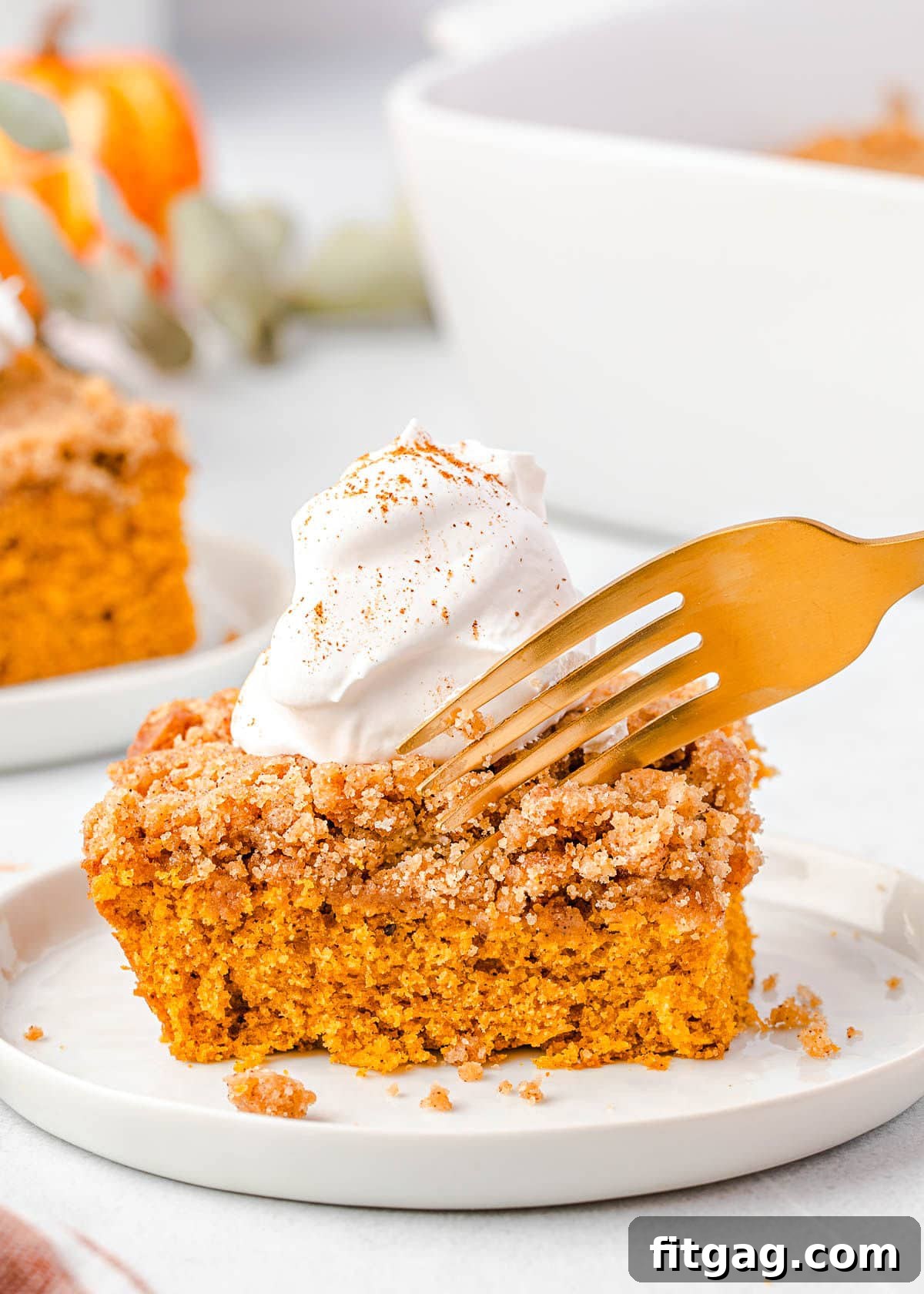 A fork poised to take a bite from a slice of moist Pumpkin Coffee Cake, topped with a generous swirl of white whipped cream, showcasing its irresistible texture and inviting flavor.